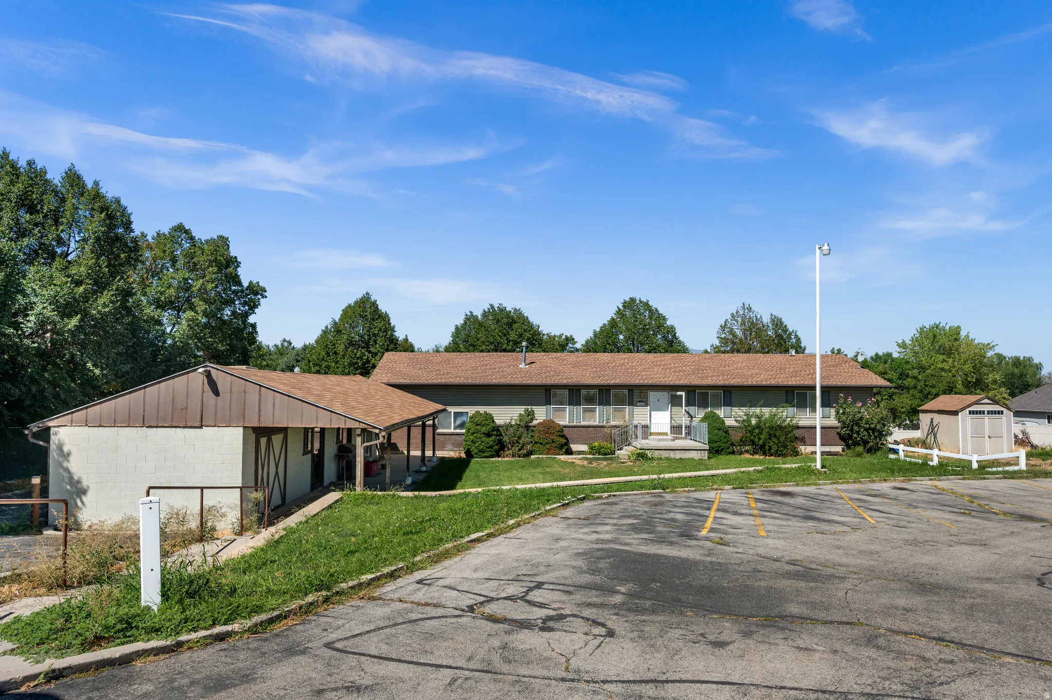 Spacious paved parking area with striping, mature perimeter trees, and a detached storage shed