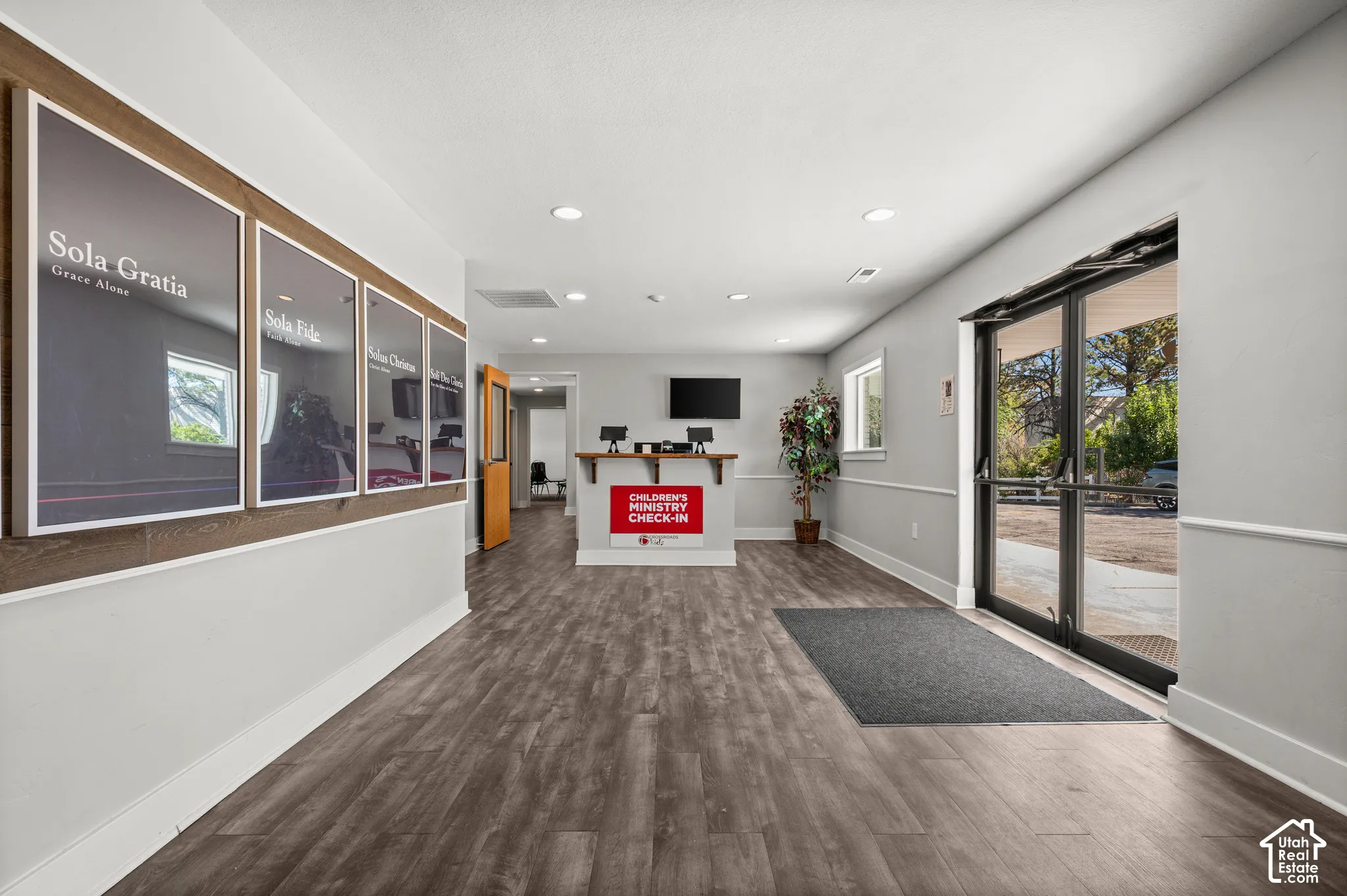 Wood-finish flooring, recessed ceiling lighting, wall-mounted display, and glass-paned double doors