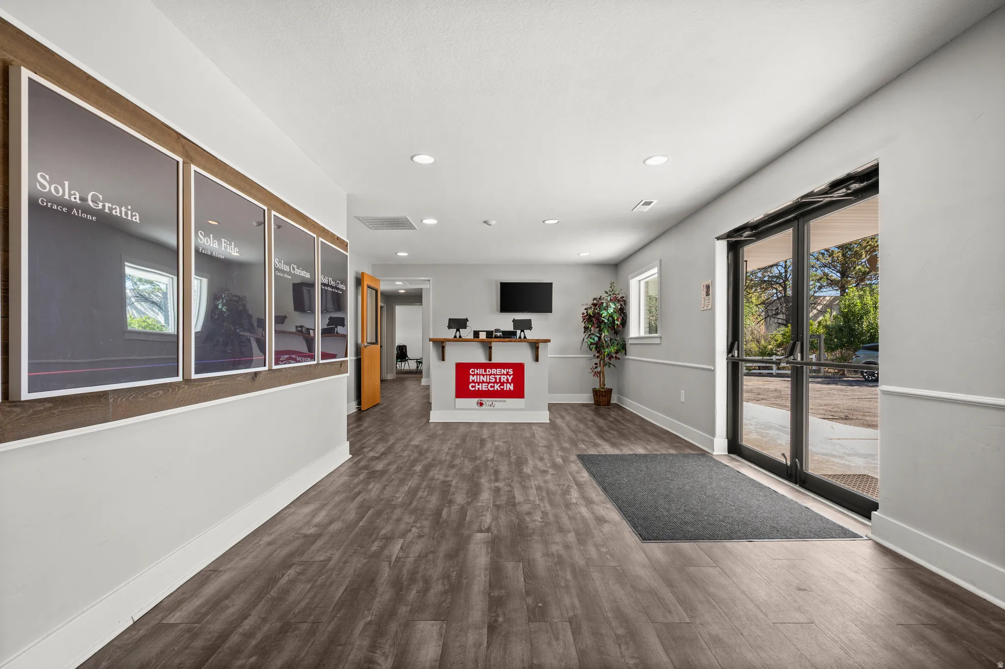Wood-finish flooring, recessed ceiling lighting, wall-mounted display, and glass-paned double doors