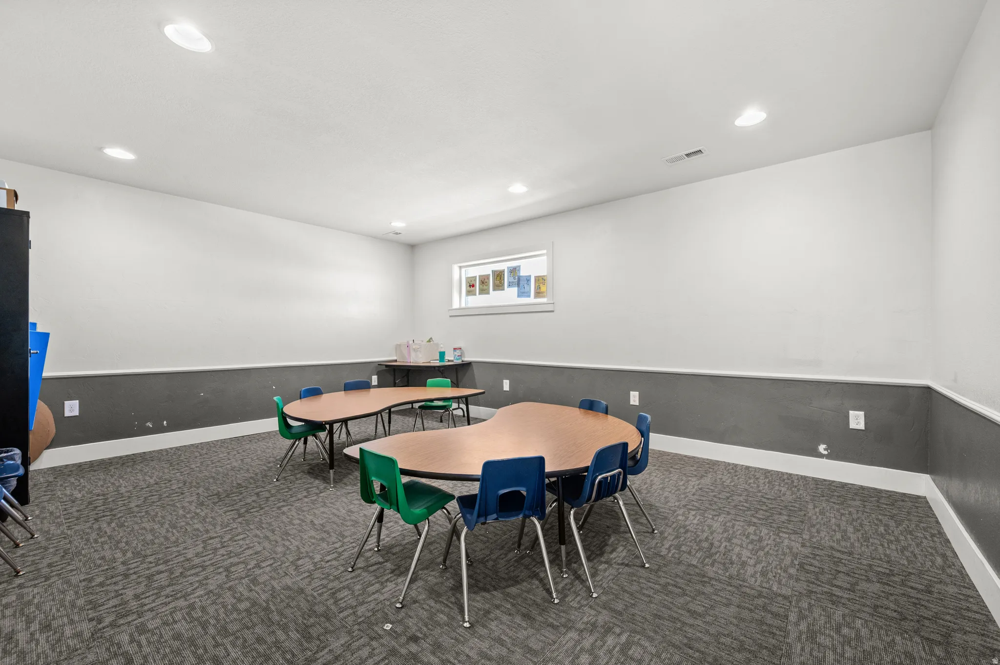 Recessed lighting illuminates a spacious room featuring a window with natural light, two-tone walls, and patterned carpet flooring