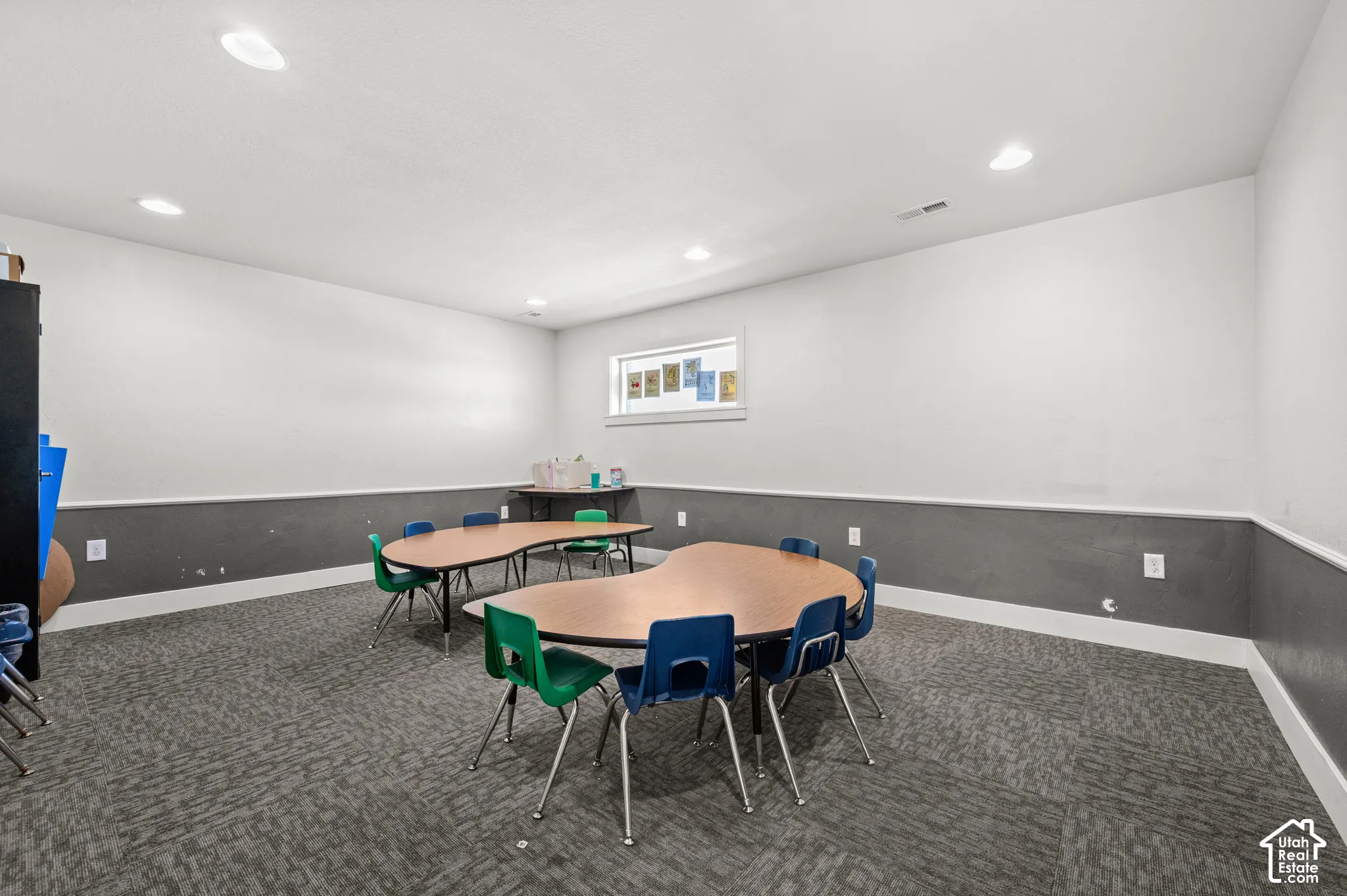 Recessed lighting illuminates a spacious room featuring a window with natural light, two-tone walls, and patterned carpet flooring