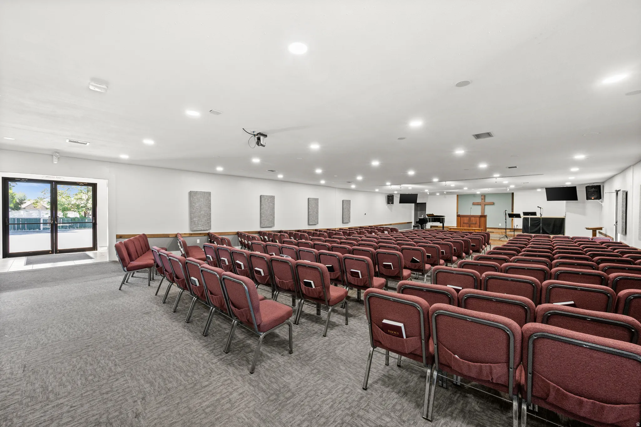 Large open space featuring recessed lighting, a raised platform with wood flooring, and double glass-paneled doors