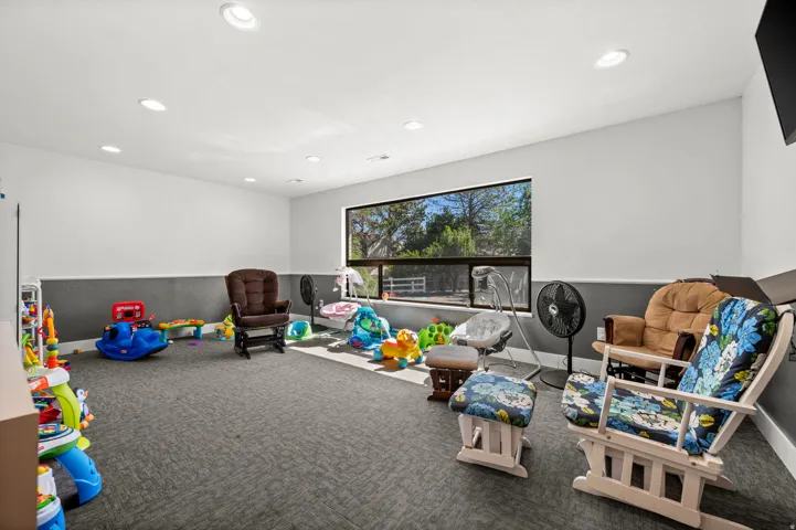 Recessed ceiling lighting illuminates a spacious room featuring a large window with a roller shade, and a textured carpeted floor