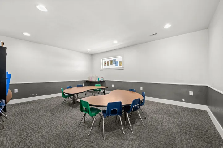 Recessed lighting illuminates a spacious room featuring a window with natural light, two-tone walls, and patterned carpet flooring