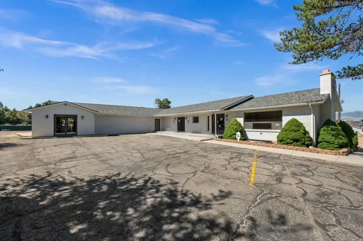 Expansive paved lot, white exterior, covered entryway, double glass doors, and a brick chimney