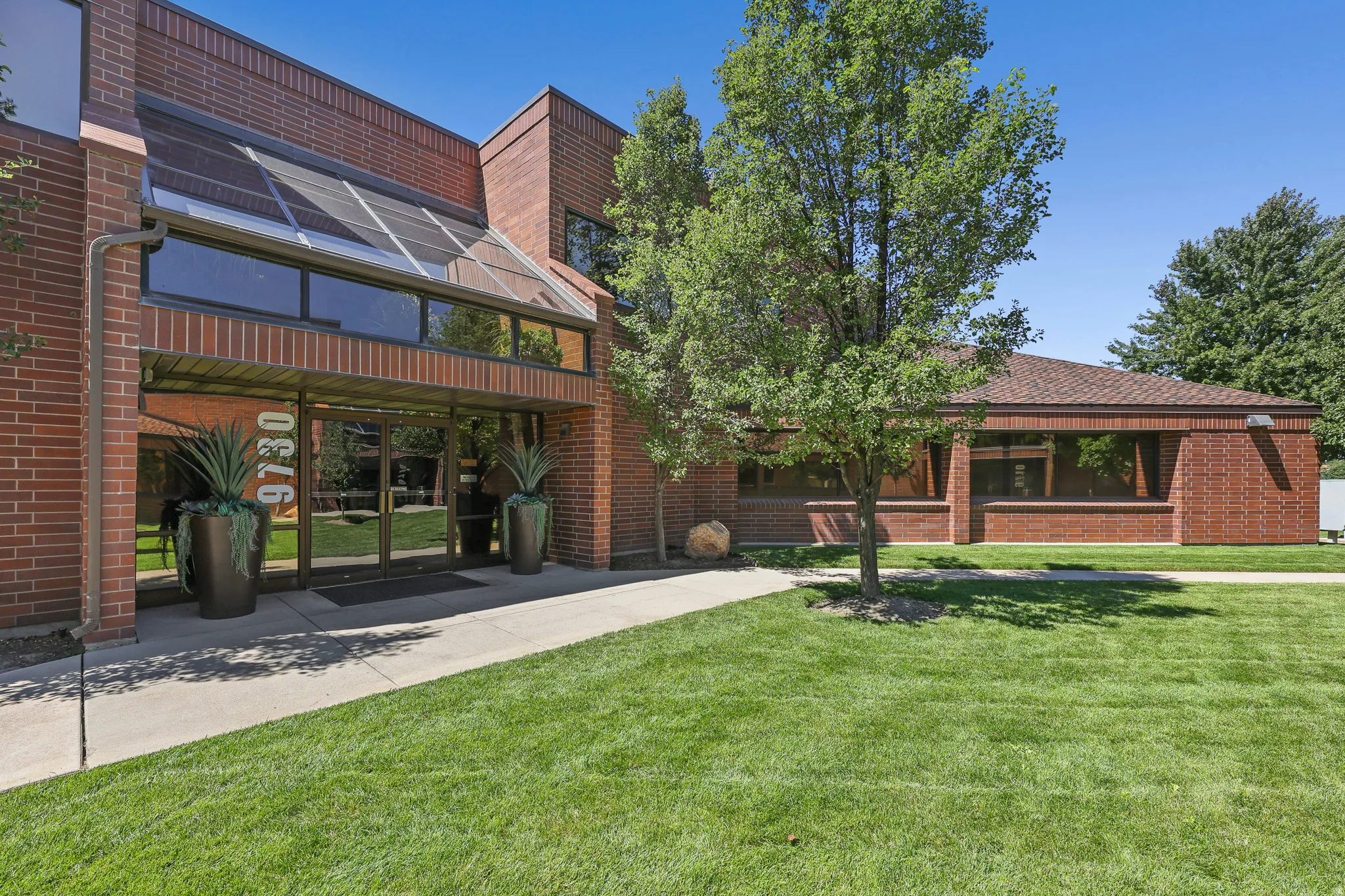 Brick exterior building with expansive glass entry, a glass-paneled awning, and a verdant lawn
