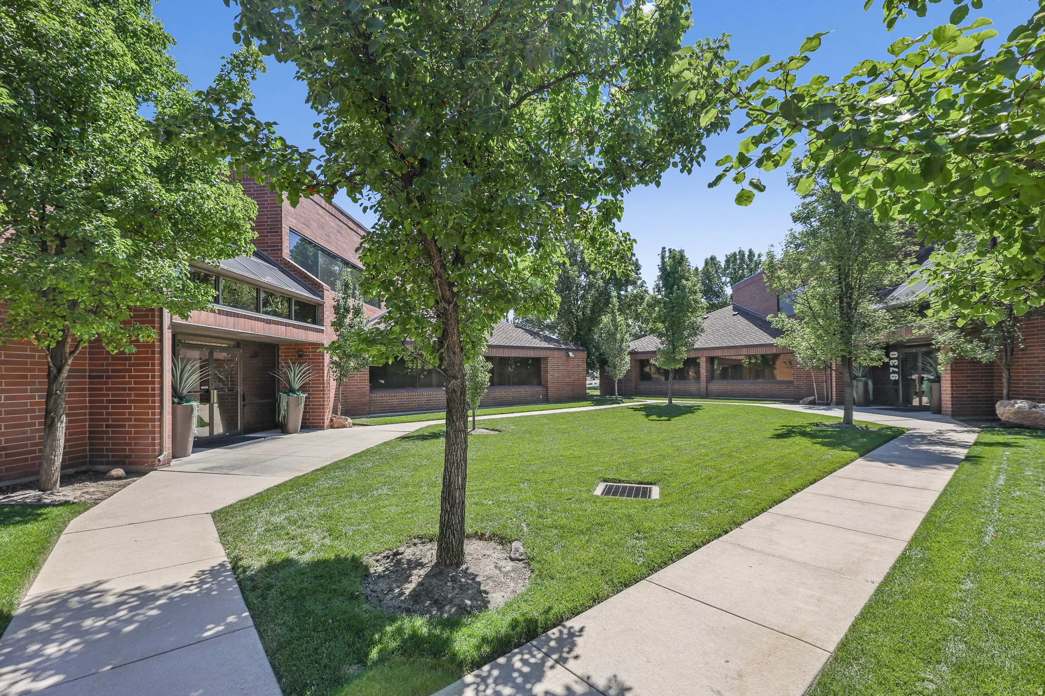 Brick exterior with multiple windows, concrete pathways, manicured lawn, and mature trees