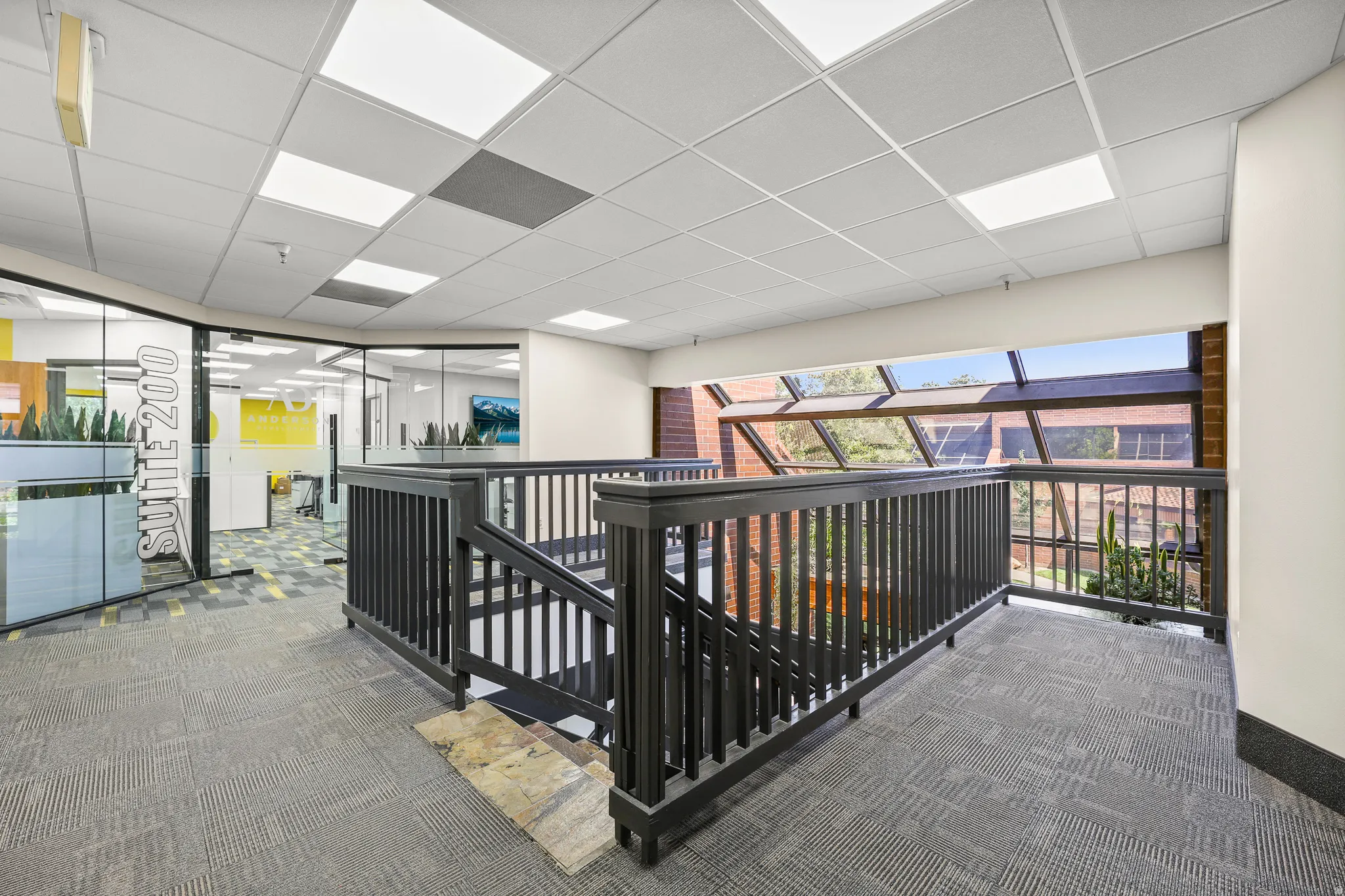 Carpeted landing with black wood railings, drop ceiling with integrated lighting, and a prominent glass window wall