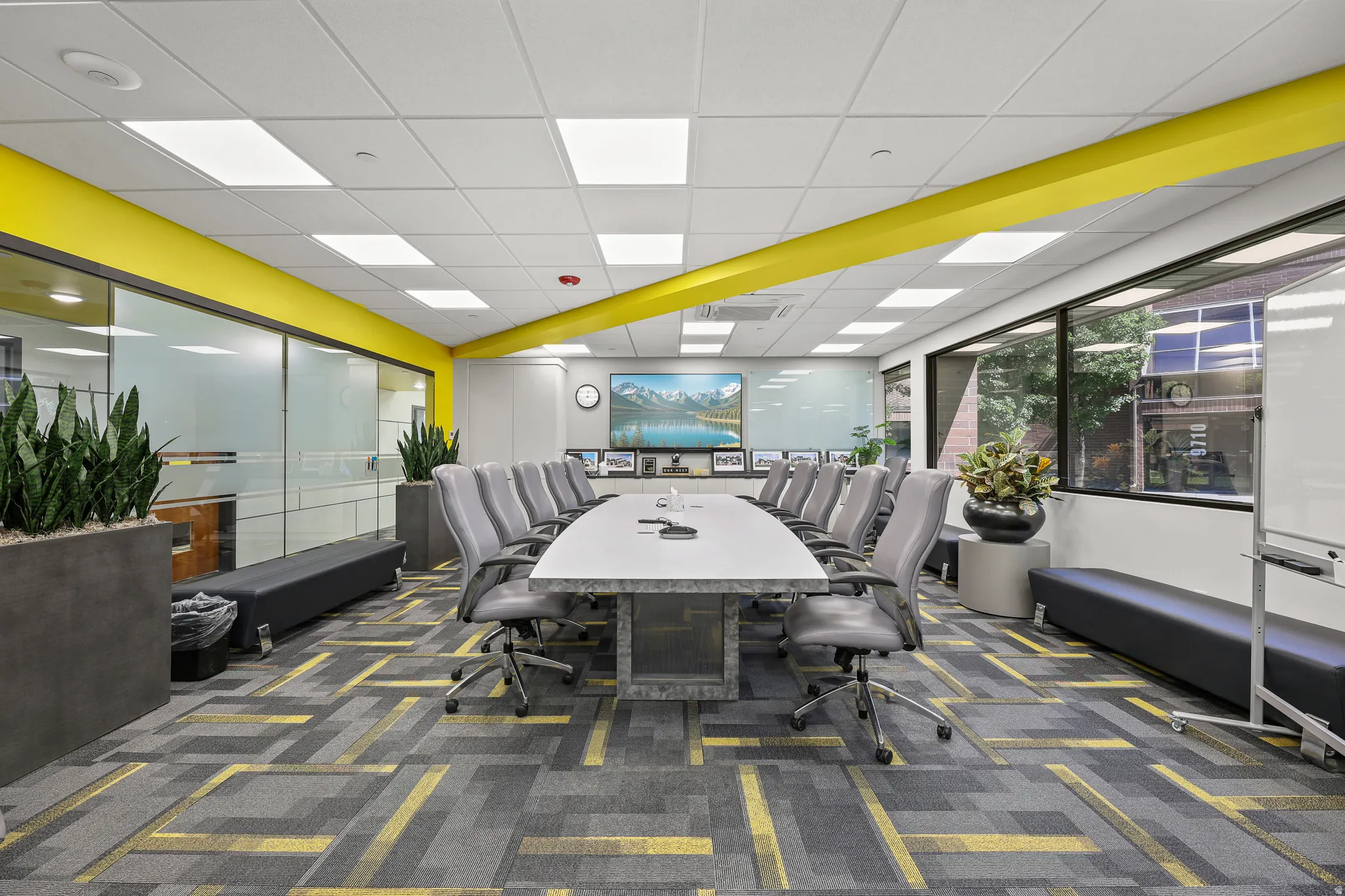 Spacious conference room featuring a large rectangular table, ample seating, expansive windows, recessed lighting, and a patterned carpet