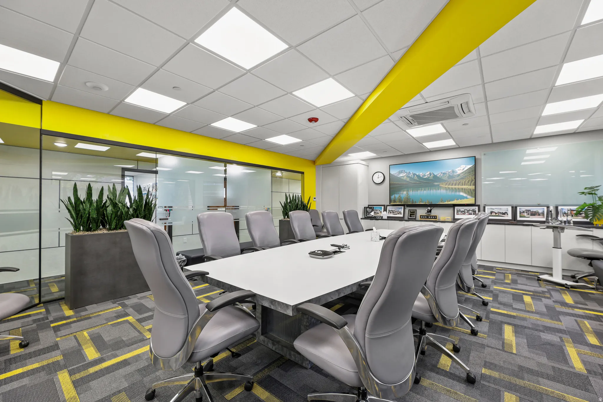 Conference room with a large screen display, expansive glass partitions, integrated ceiling lighting, built-in storage cabinetry, and patterned carpet