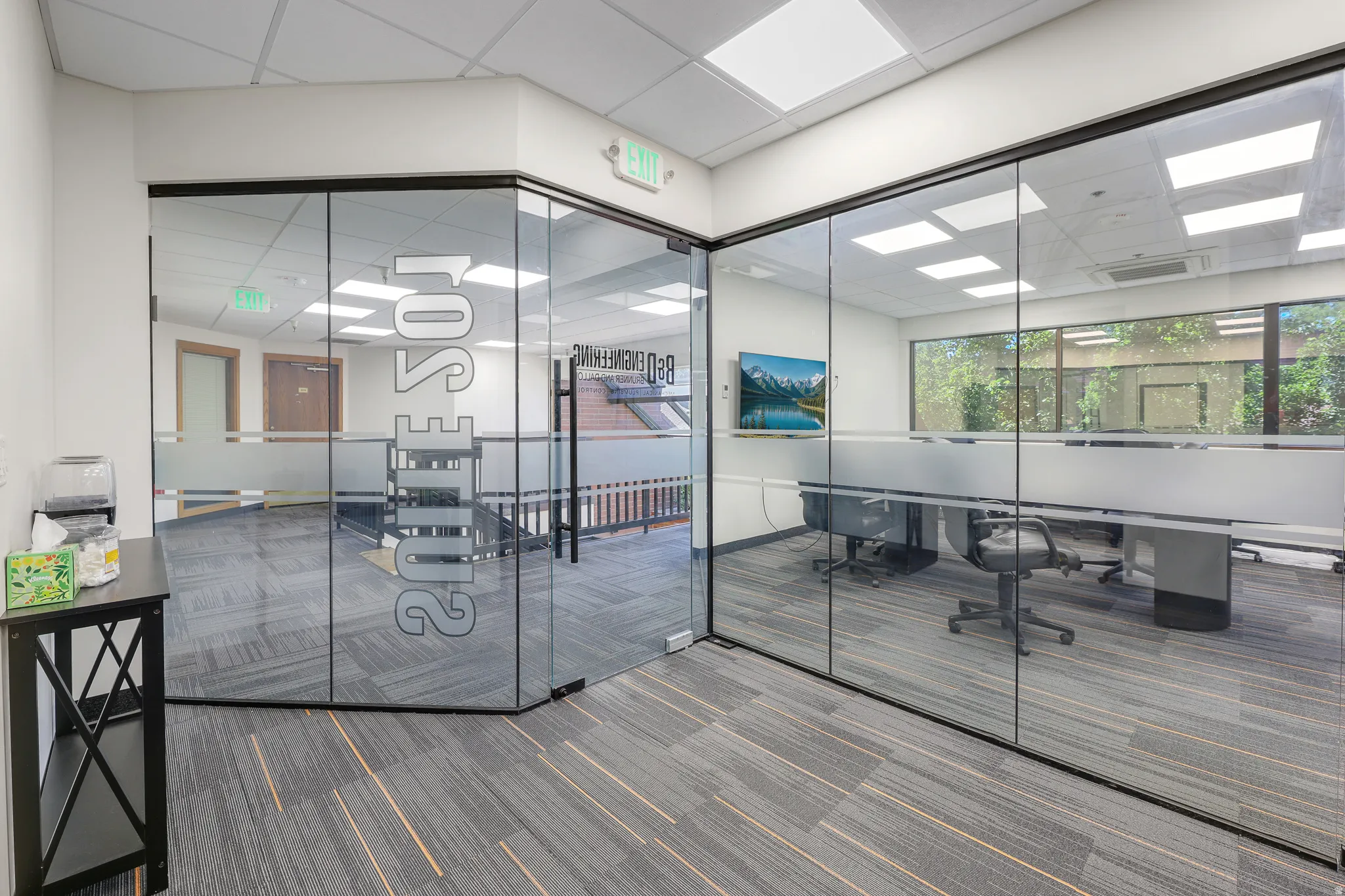 Modern office space featuring full-height glass partitions, patterned carpet flooring, and integrated ceiling lighting