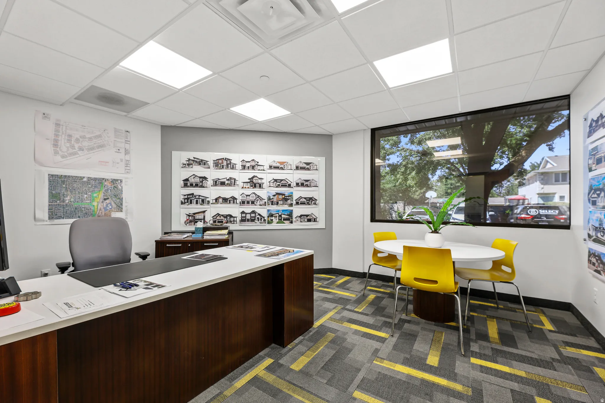 Recessed ceiling lighting, a large window, patterned carpet flooring, and a built-in desk with a light-toned countertop