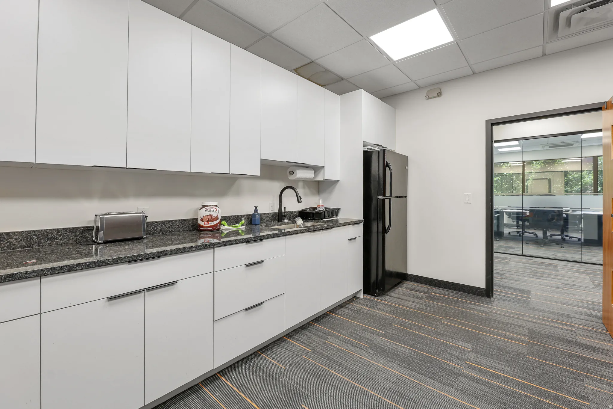 White cabinetry with modern hardware, dark stone-finish countertops, and a full-size black refrigerator