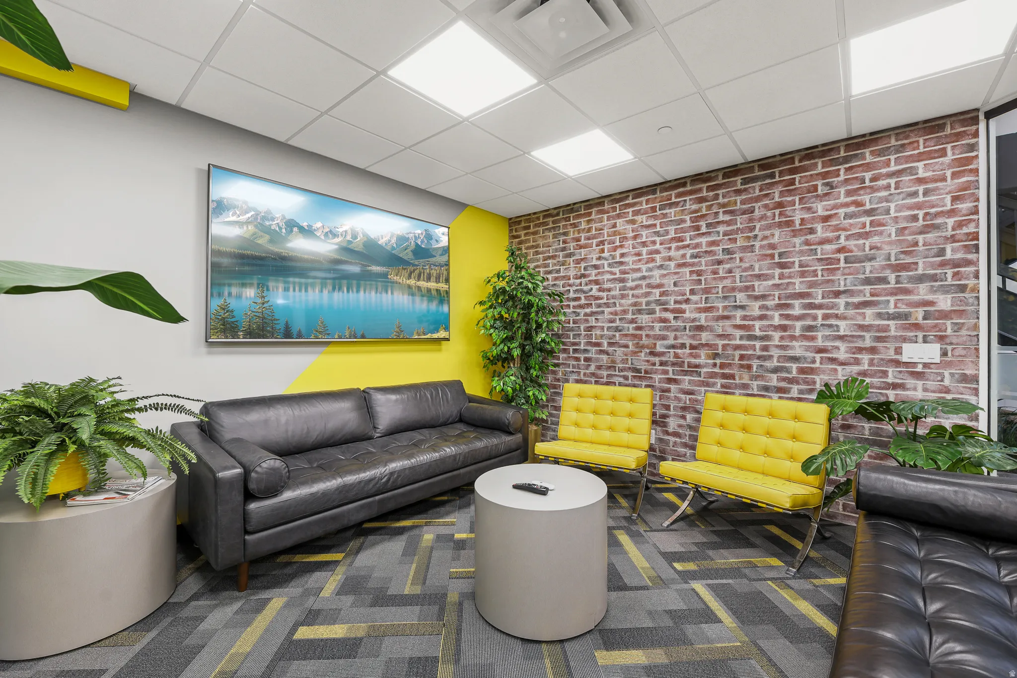 Exposed brick wall accent, dropped ceiling with integrated lighting, wall-mounted display, and patterned carpet