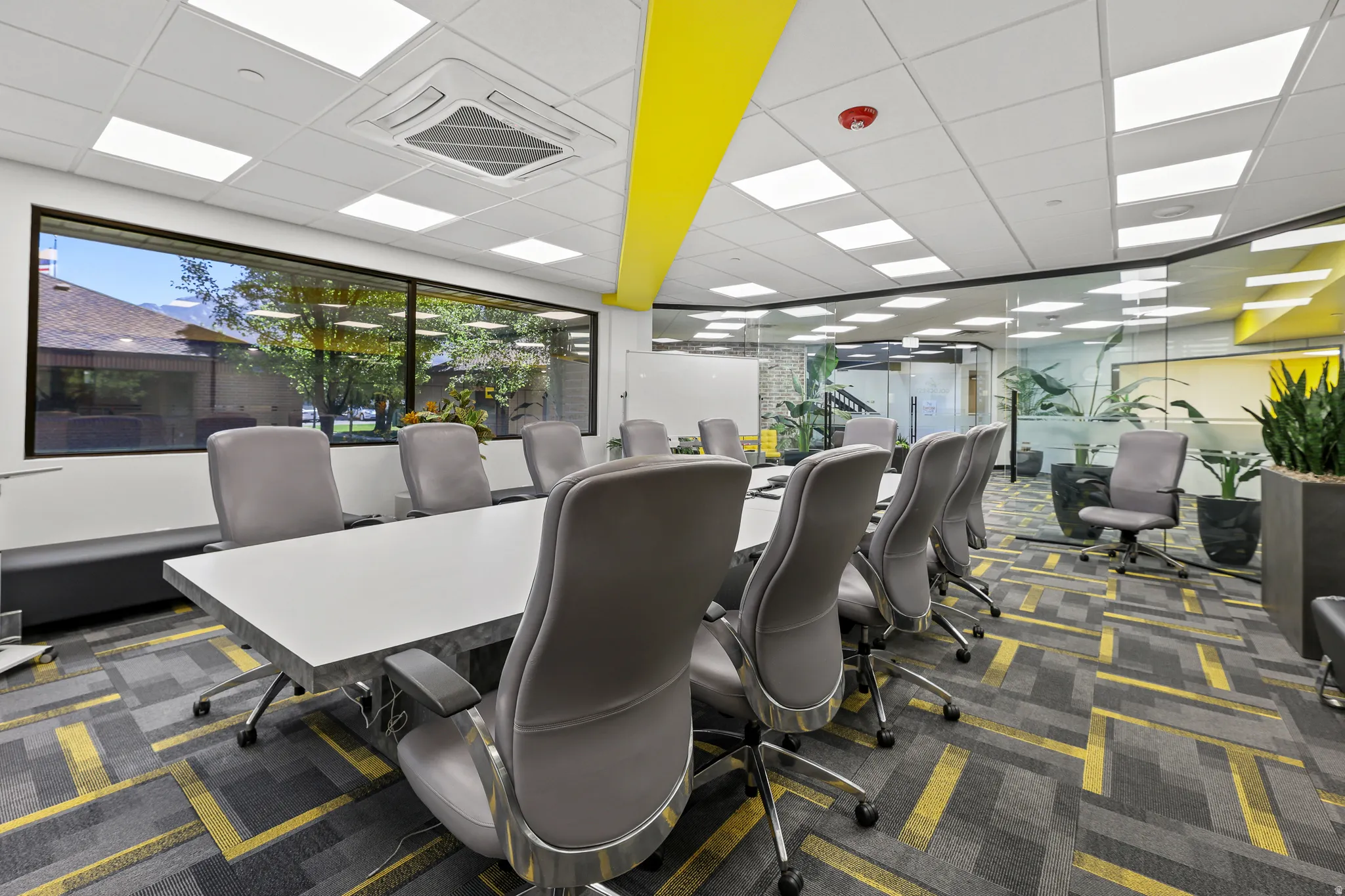 Conference room with a large rectangular table, patterned carpet flooring, extensive window line, and glass partition walls
