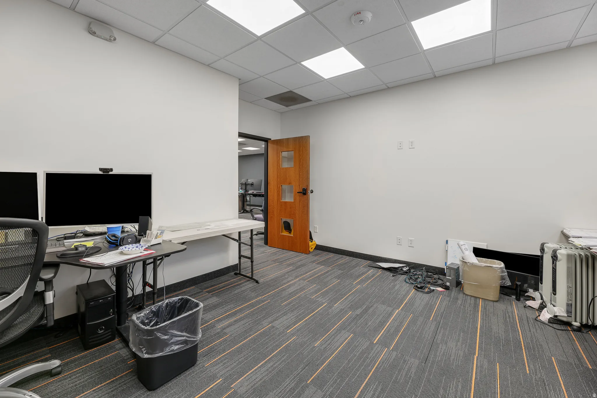 Recessed ceiling lighting, dropped ceiling, wood-finish door, patterned carpet flooring, white painted walls