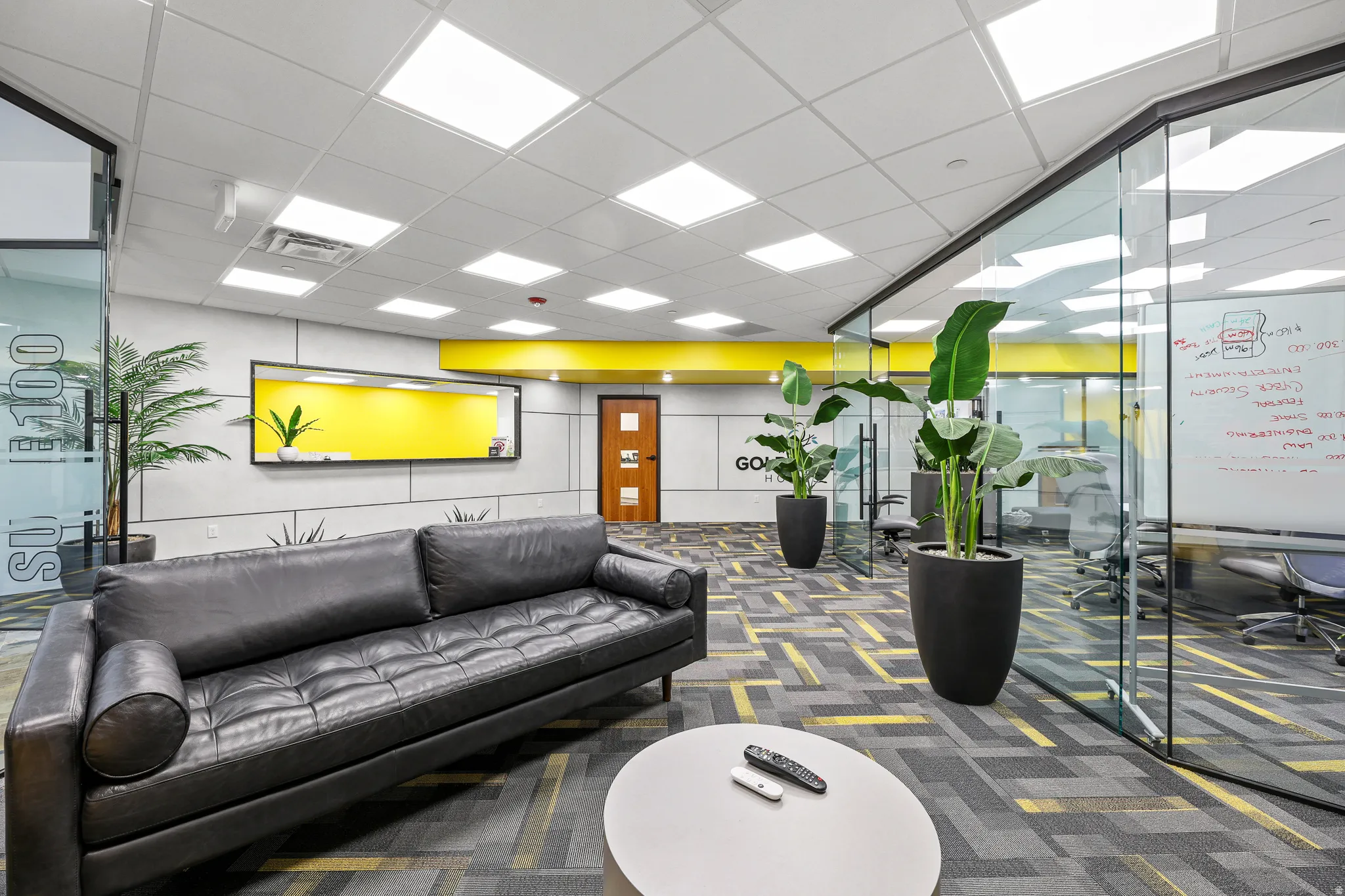 Glass partition walls, grid ceiling with integrated lighting, wood-finish door, and patterned carpet flooring