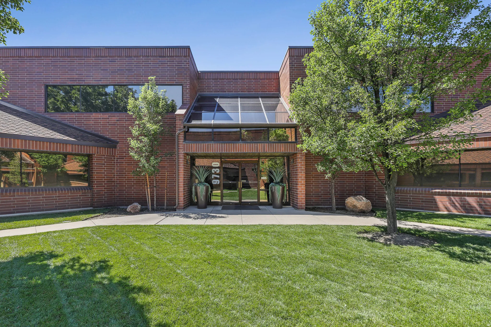 Red brick exterior with multiple windows, prominent glass entryway, and a sloped roofline