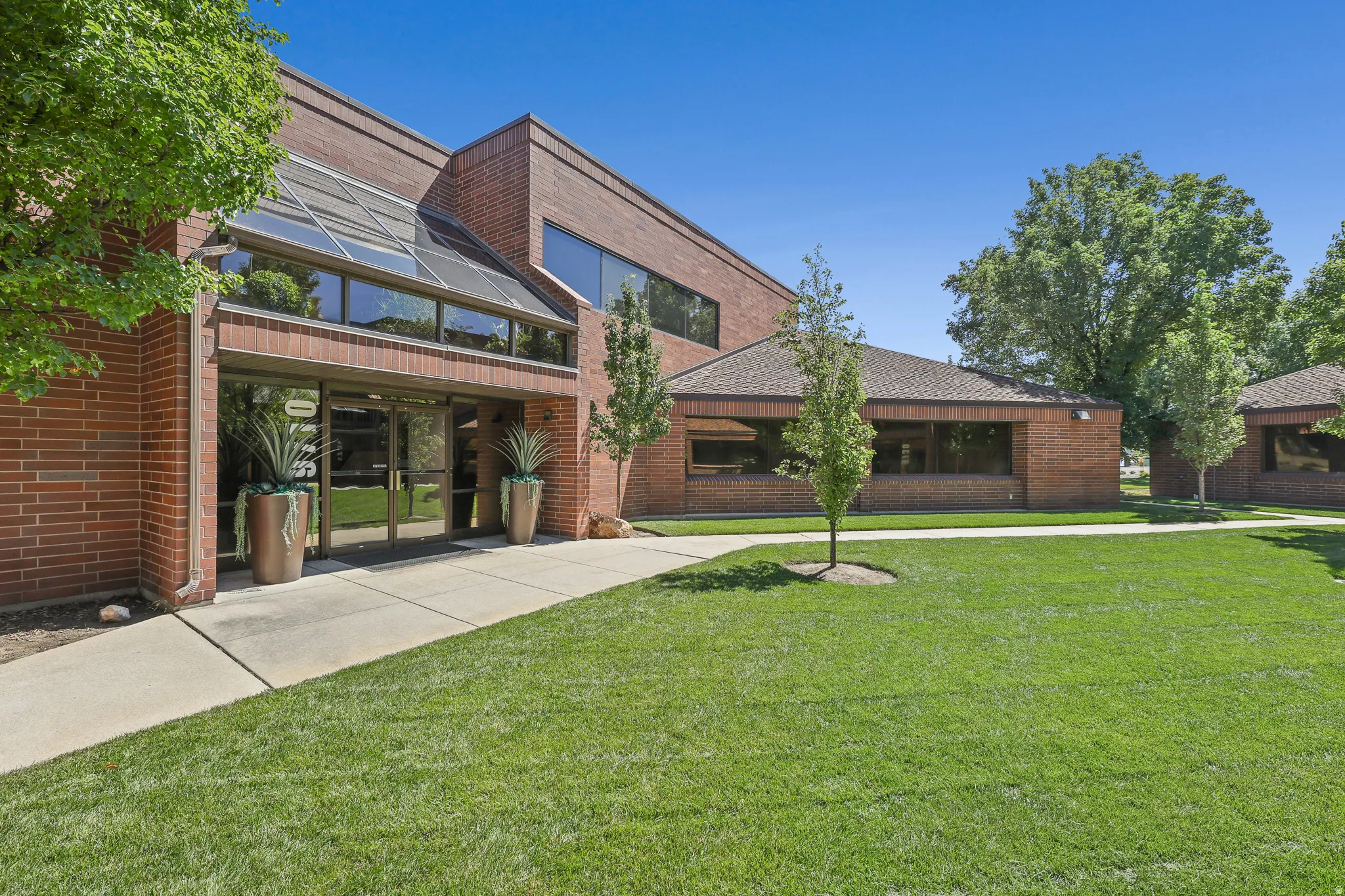 Brick exterior with large glass entry, sloped glass canopy, and surrounding green space with mature trees