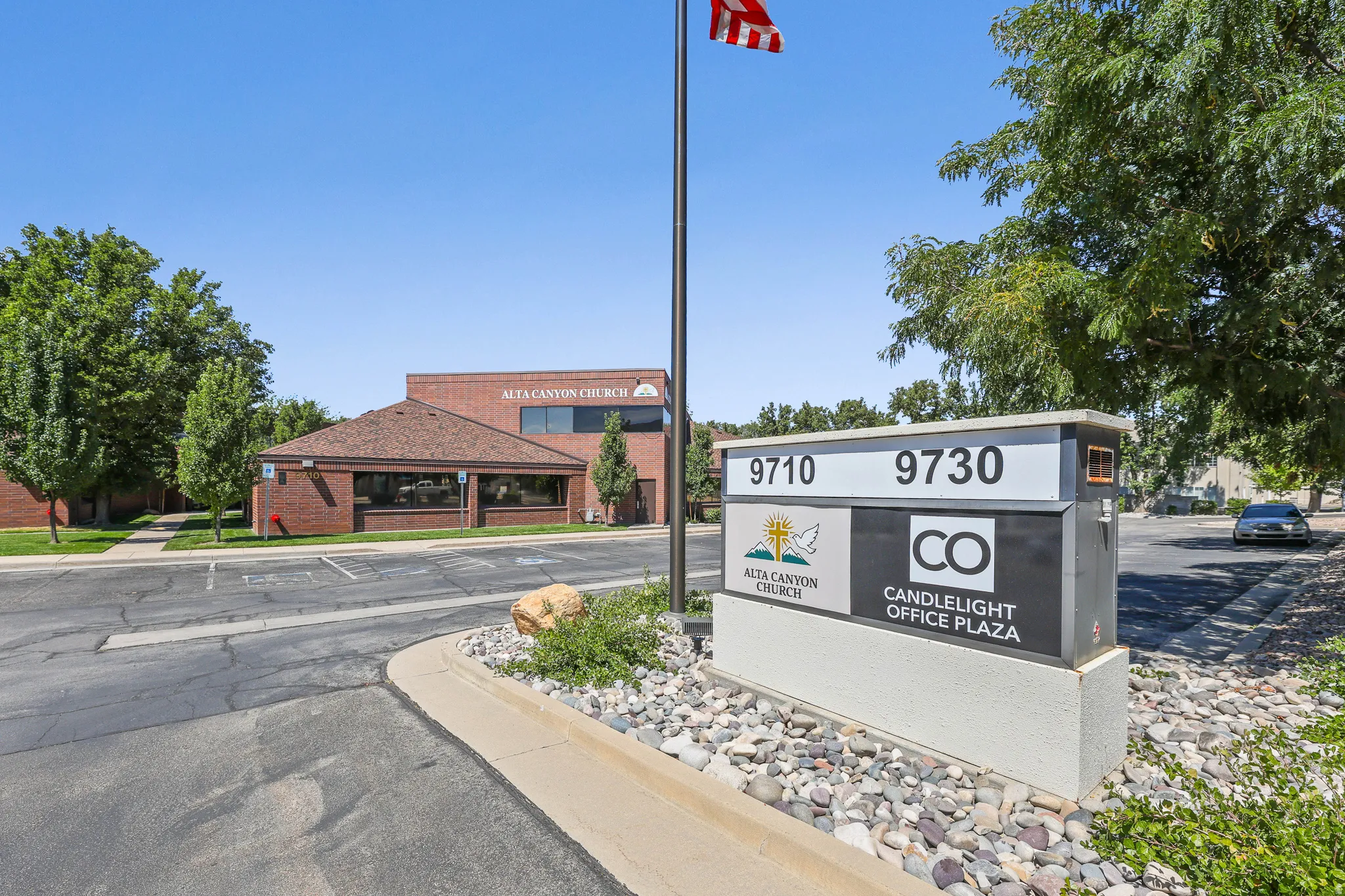 Brick commercial building with large windows, paved parking area, and mature landscaping