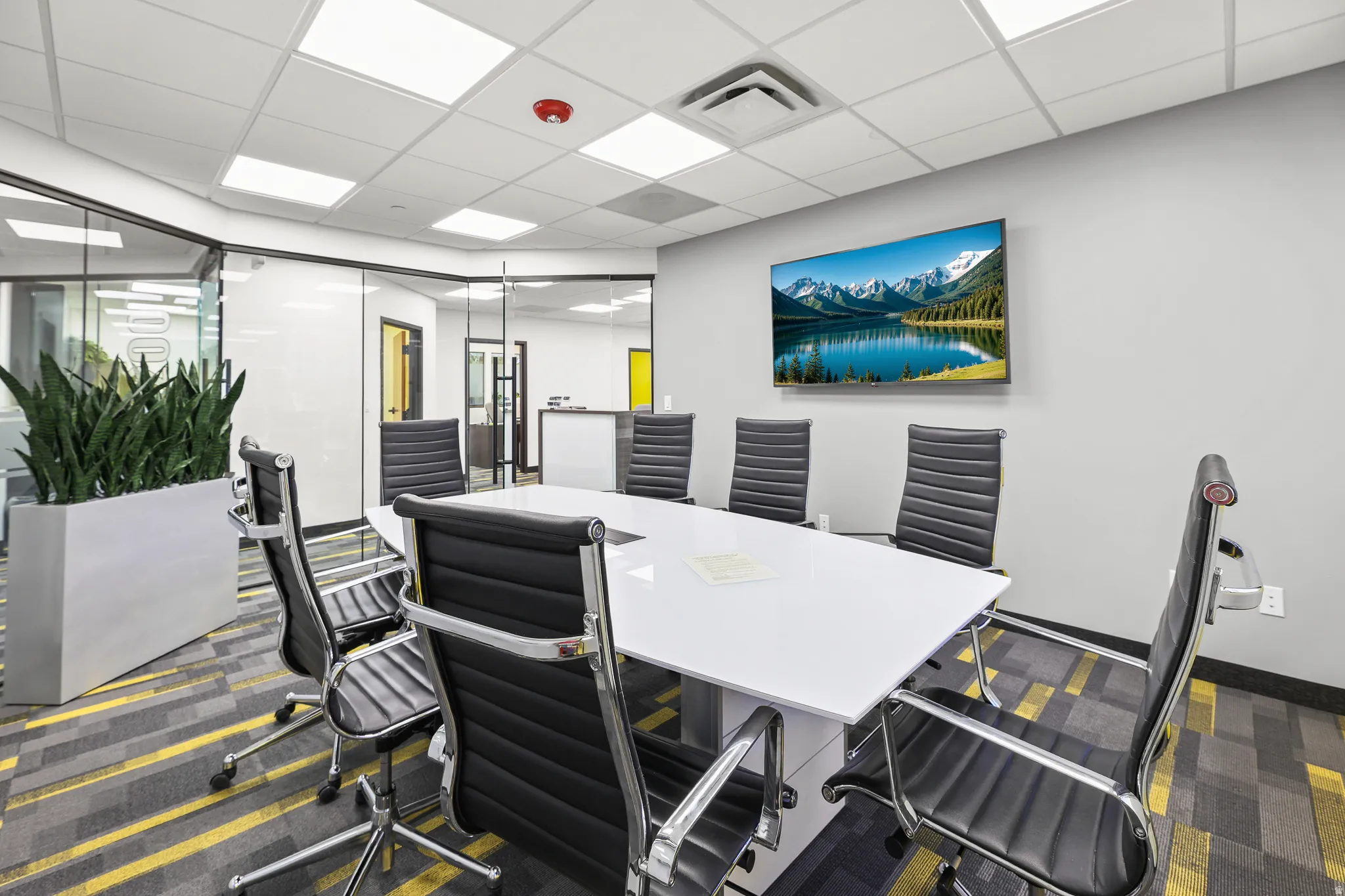 Conference room featuring a wall-mounted display, glass partition walls, and a dropped ceiling with recessed lighting
