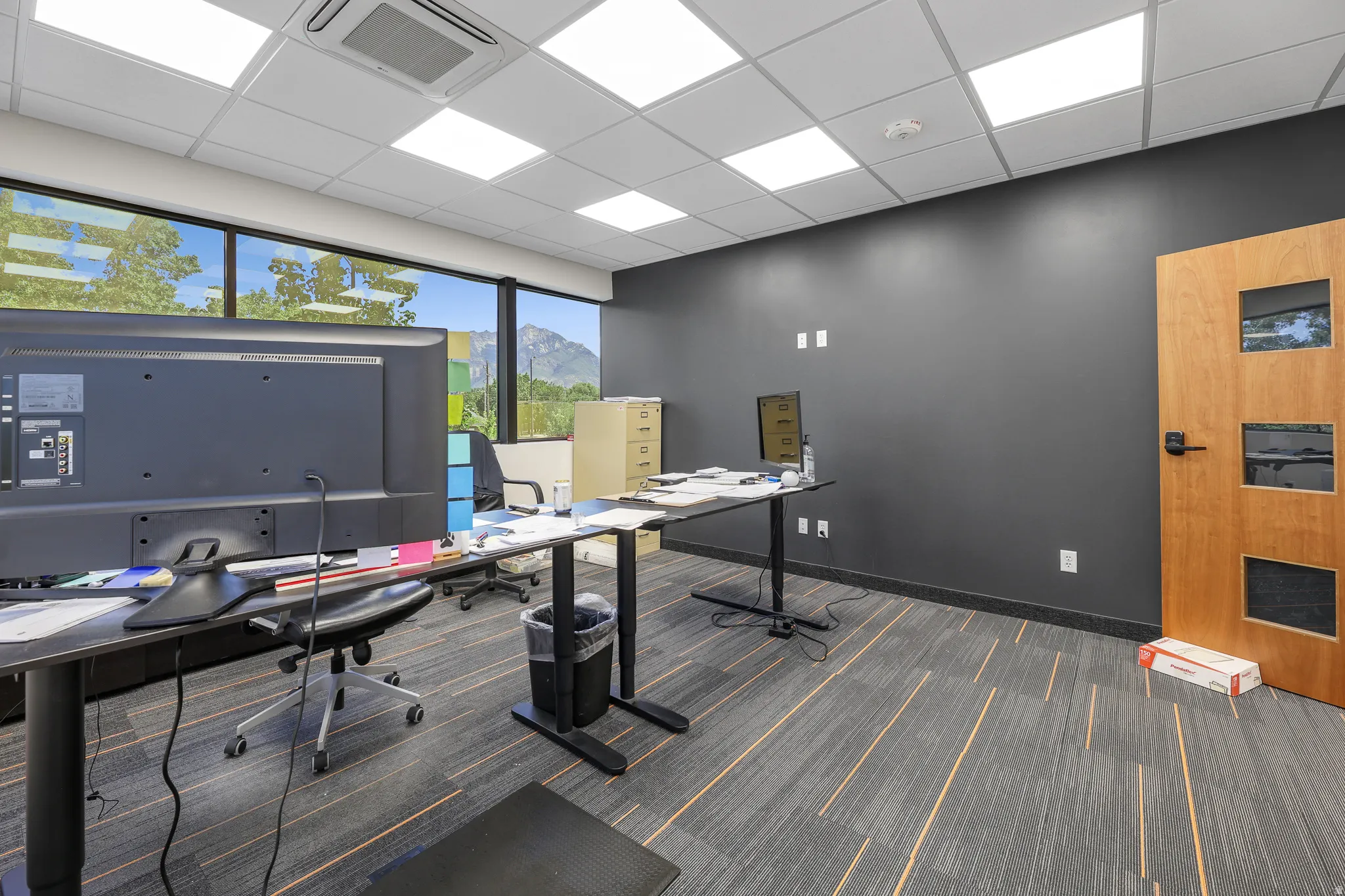 Expansive window line, acoustical tile ceiling with recessed lighting, dark accent wall, and wood-finish door with frosted panels