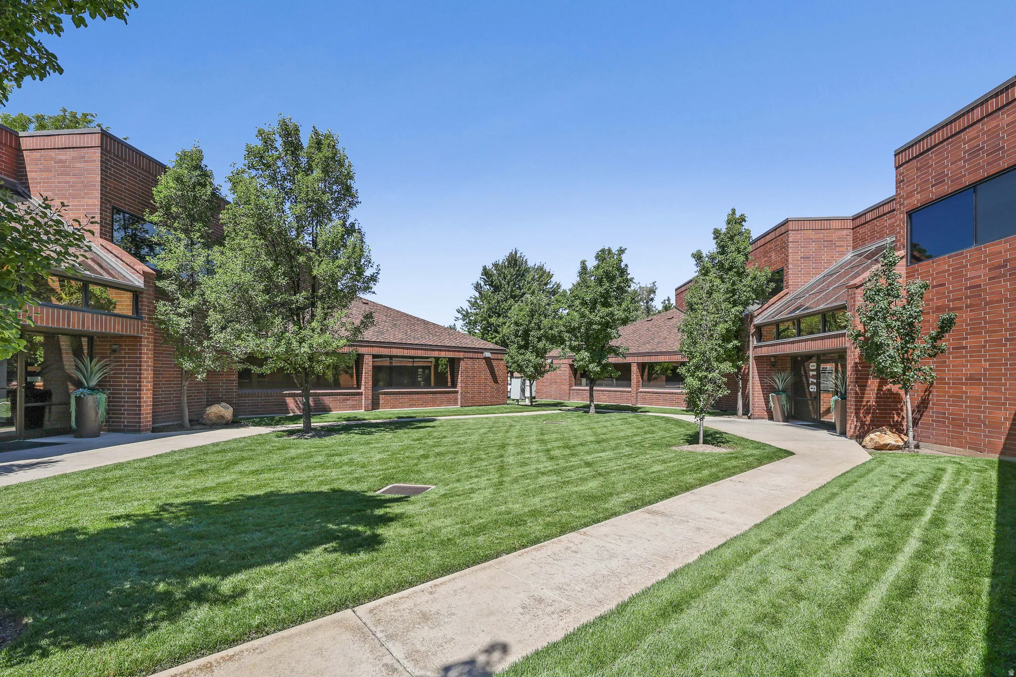 Brick exterior building with expansive lawn, mature trees, concrete pathways, and architectural glass features