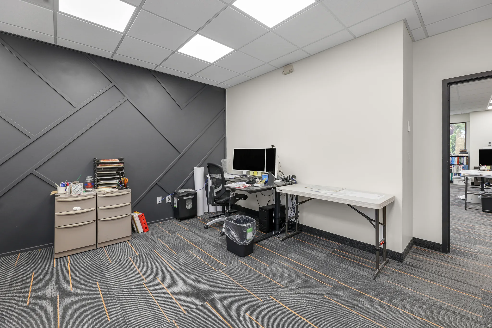 Accent wall with geometric paneling, dropped ceiling with integrated lighting, and carpet flooring with linear accents