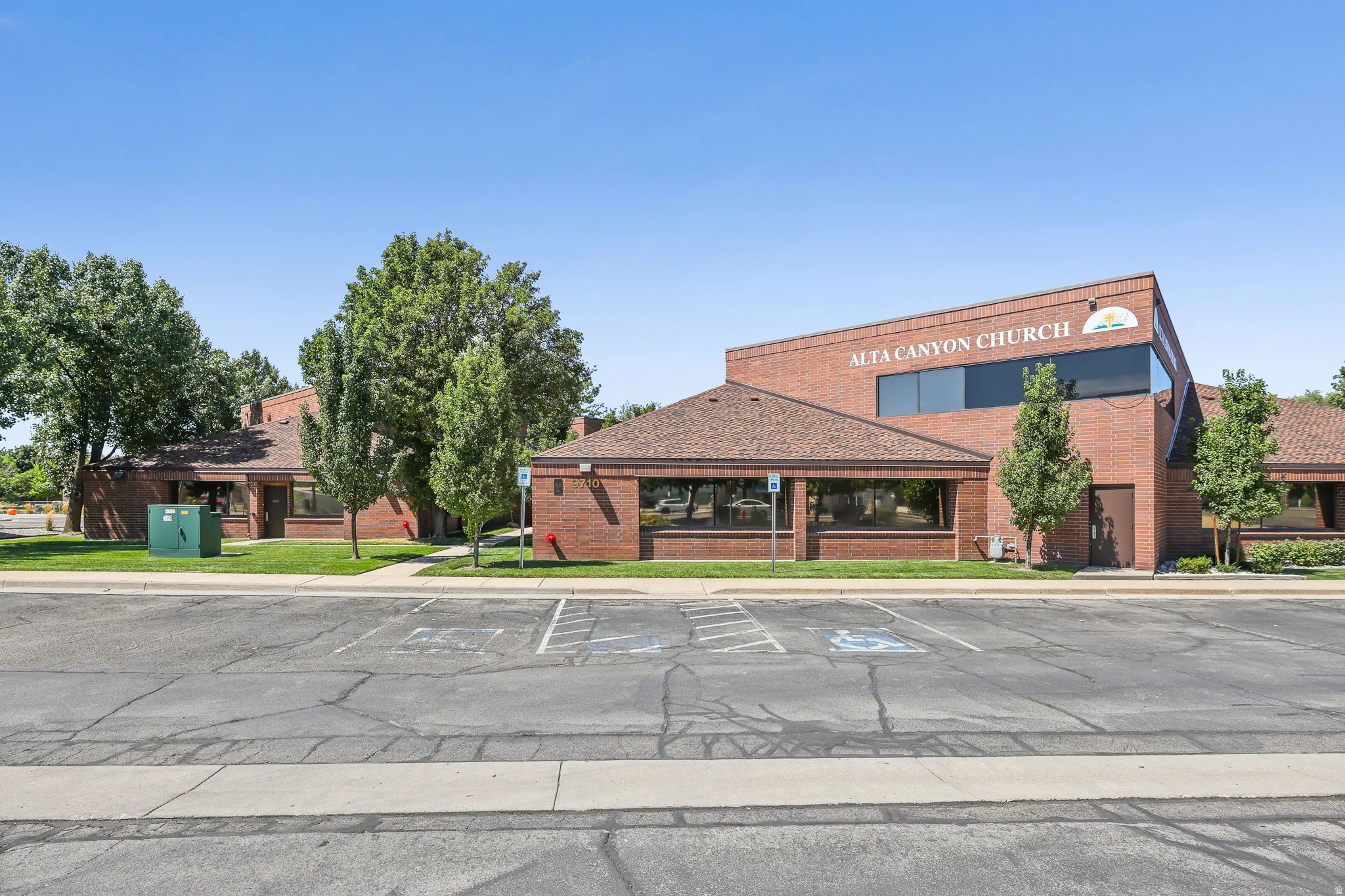 Brick exterior with a peaked roofline, multiple windows, and an asphalt parking area