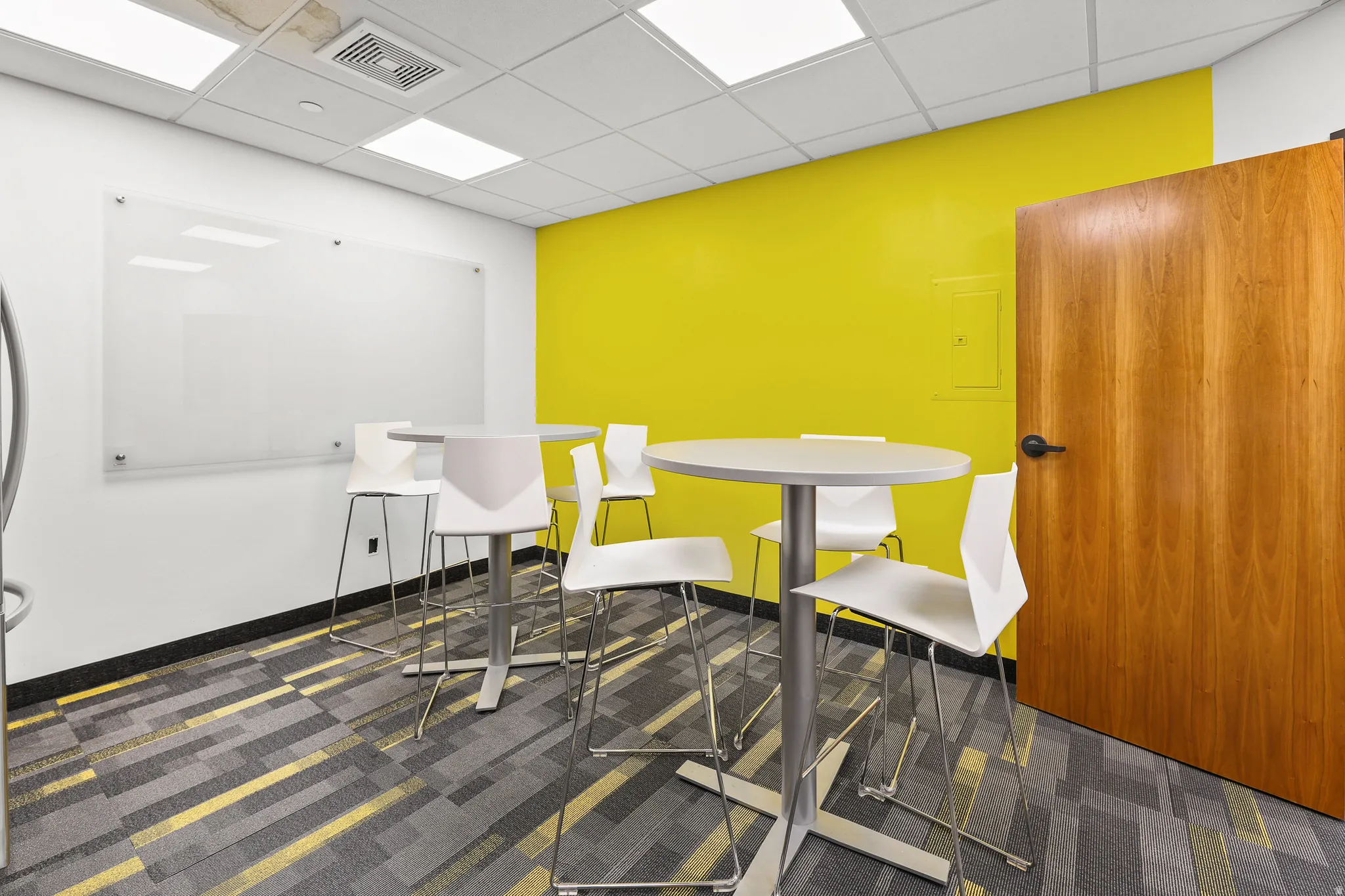 Accent wall, wood-finish door, patterned carpet flooring, suspended acoustic ceiling, and ceiling-mounted lighting