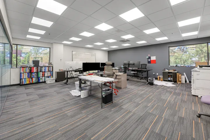 Spacious open-plan office featuring recessed lighting, large windows, and patterned carpet flooring