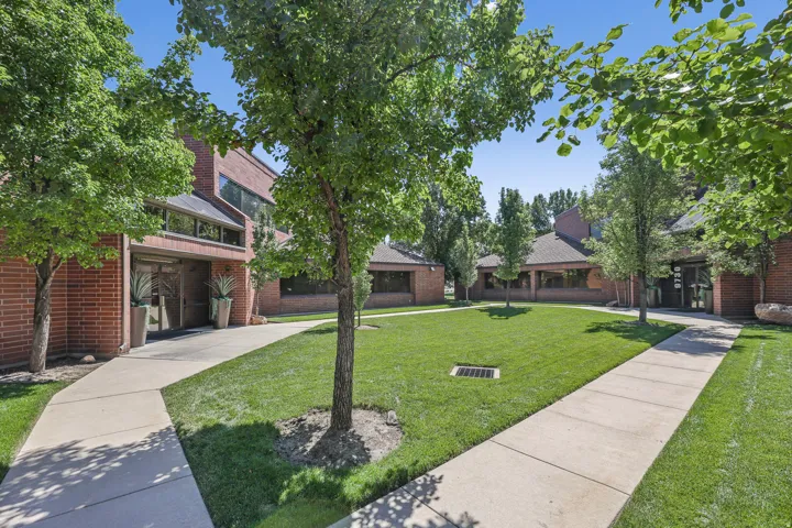 Brick exterior with multiple windows, concrete pathways, manicured lawn, and mature trees