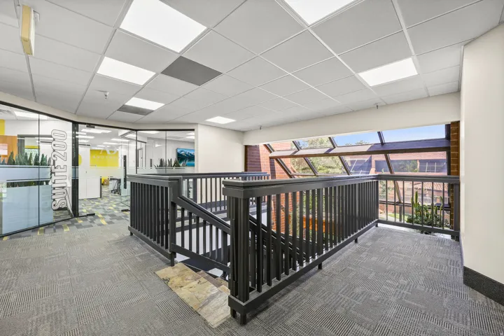 Carpeted landing with black wood railings, drop ceiling with integrated lighting, and a prominent glass window wall