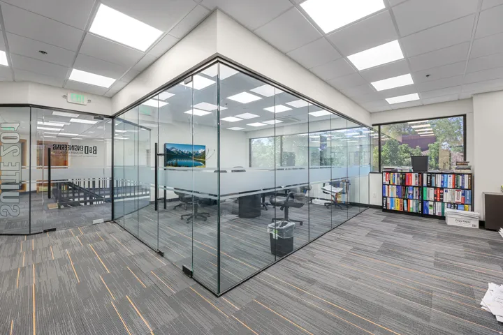 Glass-enclosed conference room with frosted privacy banding, suspended ceiling with recessed lighting, and carpet flooring