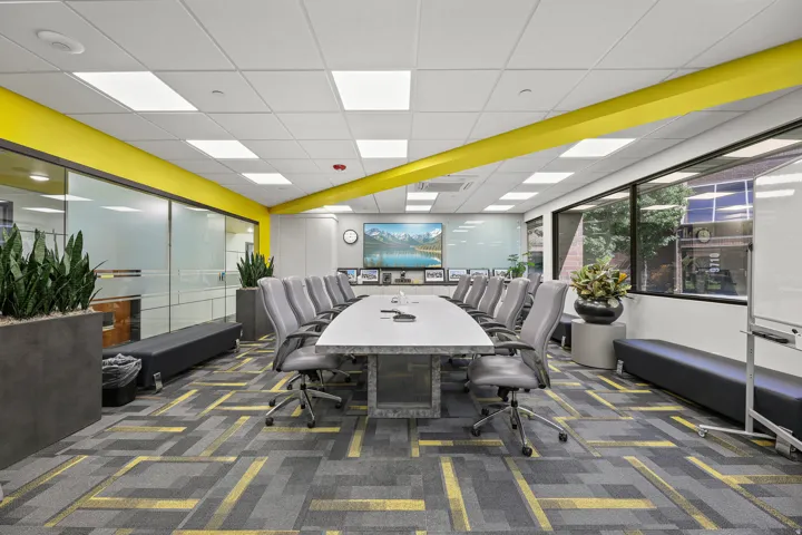 Spacious conference room featuring a large rectangular table, ample seating, expansive windows, recessed lighting, and a patterned carpet