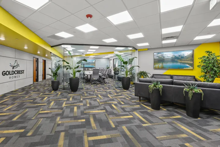 Open-plan commercial space featuring patterned carpeting, recessed ceiling lighting, a glass-partitioned conference room, and a distinct accent wall