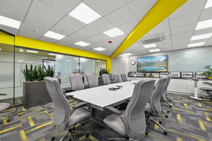 Conference room with a large screen display, expansive glass partitions, integrated ceiling lighting, built-in storage cabinetry, and patterned carpet