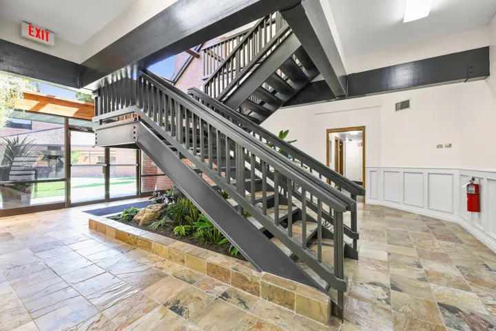 Multi-level staircase with dark wood-finish railings, stone-tile flooring, full-height window panels, and interior landscaping