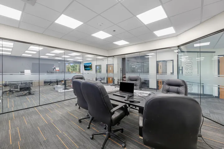 Glass-enclosed office space with carpet flooring, suspended ceiling with recessed lighting, and a wall-mounted display