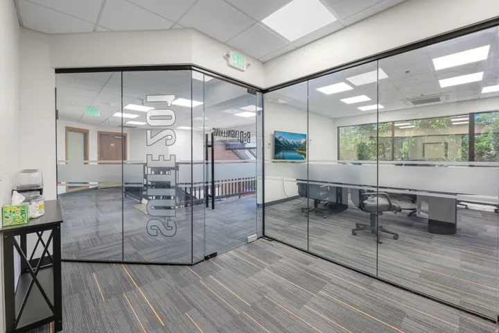 Modern office space featuring full-height glass partitions, patterned carpet flooring, and integrated ceiling lighting