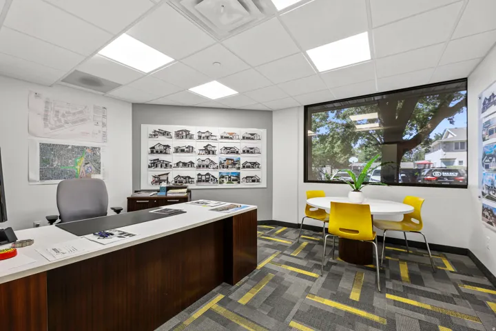 Recessed ceiling lighting, a large window, patterned carpet flooring, and a built-in desk with a light-toned countertop
