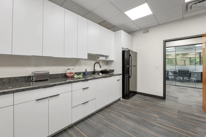 White cabinetry with modern hardware, dark stone-finish countertops, and a full-size black refrigerator