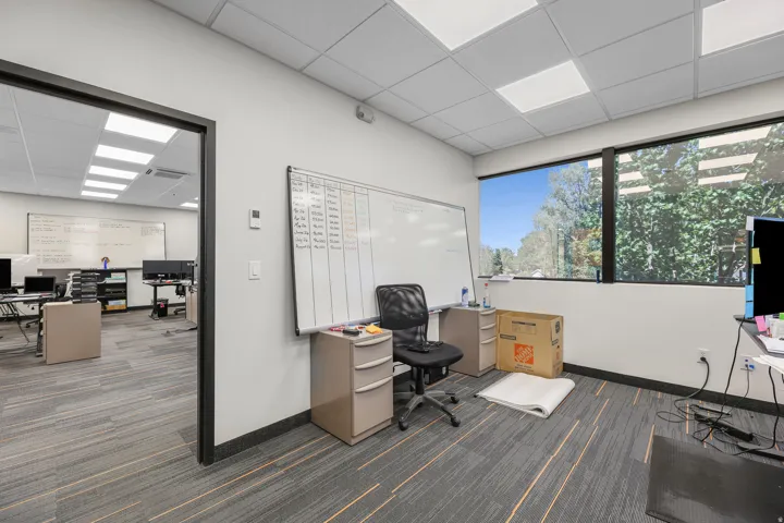 Expansive windows, drop ceiling with recessed lighting, wall-mounted whiteboard, and carpet tile flooring