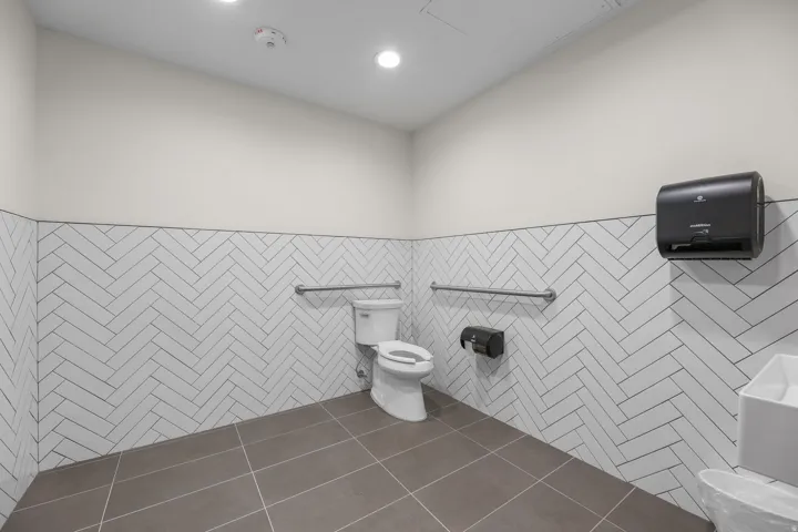 Herringbone tile wainscoting, recessed lighting, wall-mounted paper towel dispenser, stainless steel grab bars, and large format floor tiling