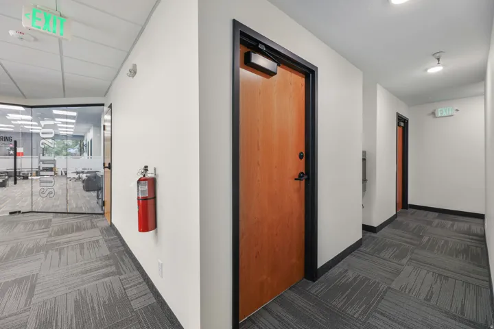 Commercial hallway with patterned carpet tile flooring, recessed ceiling lighting, and solid core doors