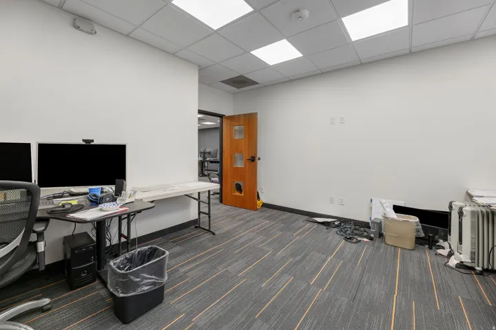 Recessed ceiling lighting, dropped ceiling, wood-finish door, patterned carpet flooring, white painted walls