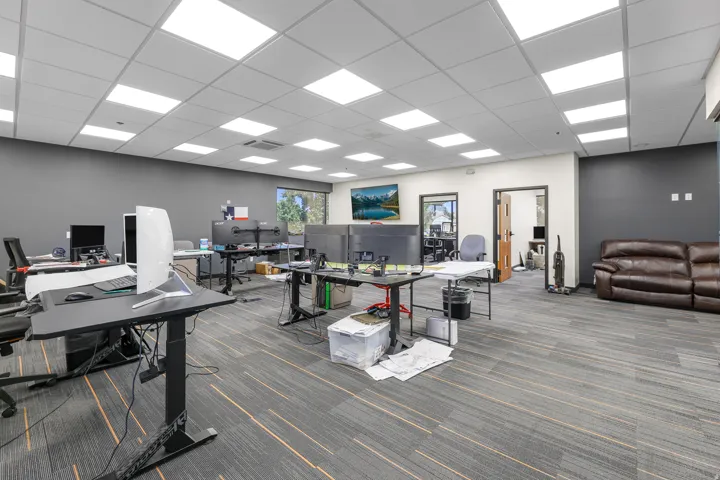 Open-plan office space featuring carpeted flooring with linear accents, suspended acoustical ceiling, recessed lighting, and a large window