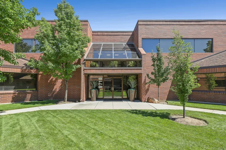 Brick exterior with a glass-enclosed entry, expansive windows, mature trees, and a concrete walkway