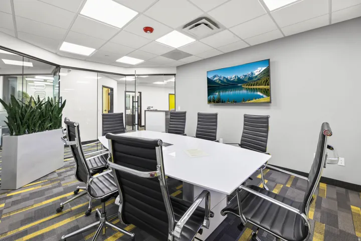 Conference room featuring a wall-mounted display, glass partition walls, and a dropped ceiling with recessed lighting