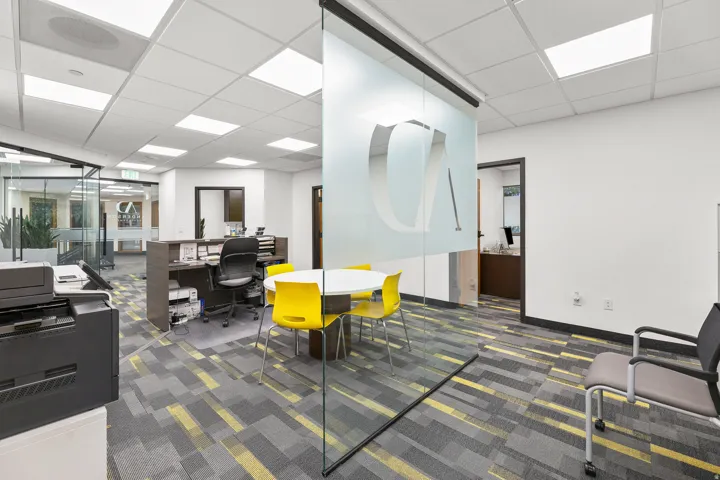 Open office space featuring patterned carpet flooring, overhead lighting, glass partition with frosted design, and reception desk